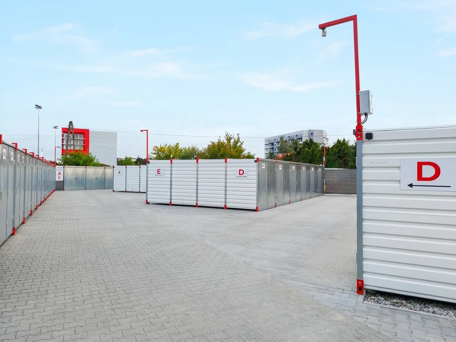 Plac z rzędami białych kontenerów magazynowych Box-Storage oznaczonych literami, z kostki brukowej
