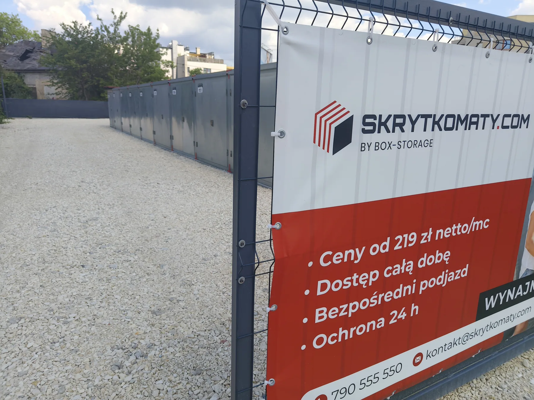 Plac Skrytkomaty przy Wojciechowskiego 4 w Ursusie: rząd skrytek i baner z cenami na ogrodzeniu